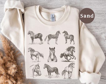 May include: A sand-colored sweatshirt featuring a collection of nine detailed horse illustrations in shades of gray. The horses are depicted in various poses, including standing, running, and portraits. The sweatshirt has long sleeves and a crew neck.