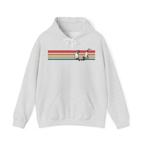 May include: A light gray hoodie with a kangaroo pocket and drawstring hood. The front features a horizontal design with red, orange, and green stripes, and two Siamese cats. The cats are in a playful pose.
