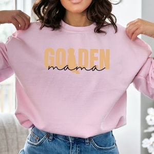 May include: A pink sweatshirt with the text "Golden mama" in orange and black lettering.
