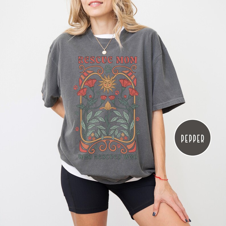 May include: A gray t-shirt with a graphic design featuring a sun, flowers, and the text "Rescue Mom Who Rescued Who".