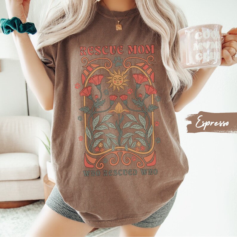 May include: A brown t-shirt with a graphic design featuring a sun, flowers, and the text "Rescue Mom Who Rescued Who".