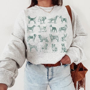May include: A gray sweatshirt with a graphic print of various dog breeds in a teal color. The sweatshirt has a relaxed fit and a crew neck.