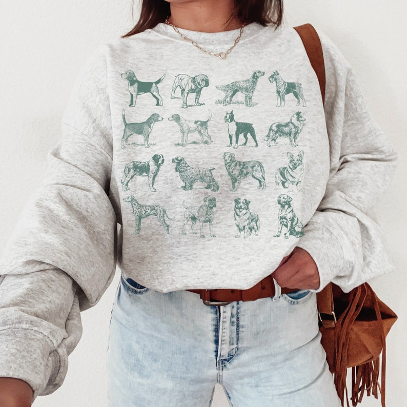 May include: A gray sweatshirt with a graphic print of various dog breeds in a teal color. The sweatshirt has a relaxed fit and a crew neck.