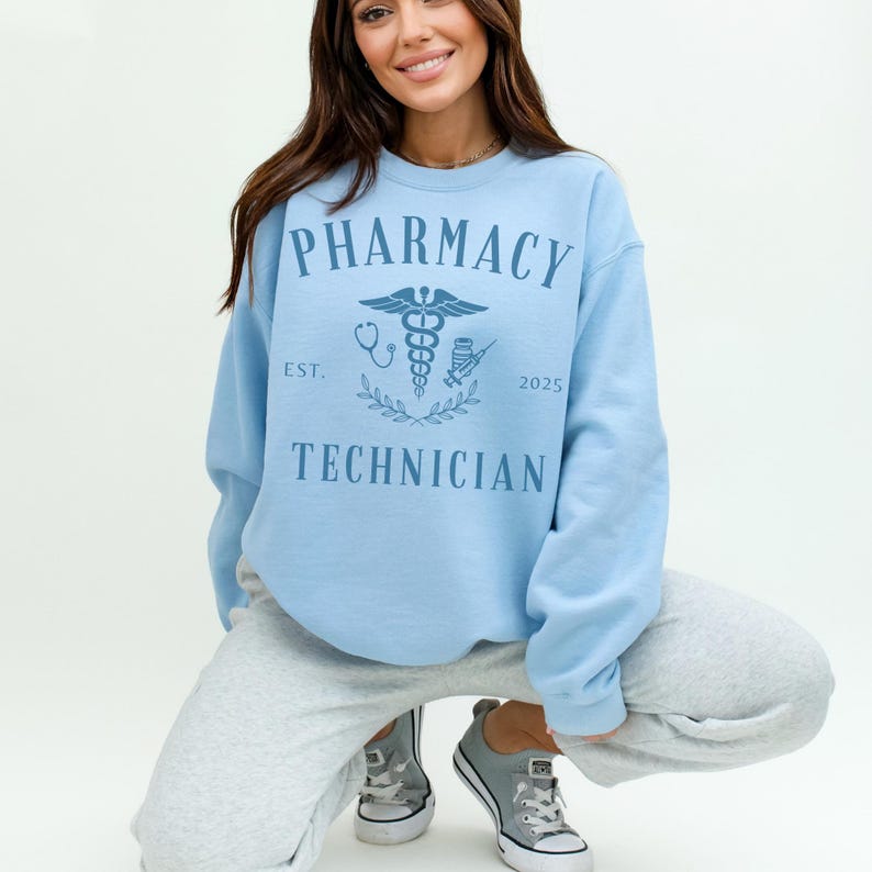 May include: Light blue sweatshirt with the text "Pharmacy Technician" and a caduceus symbol. The text "Est. 2025" is below the symbol.