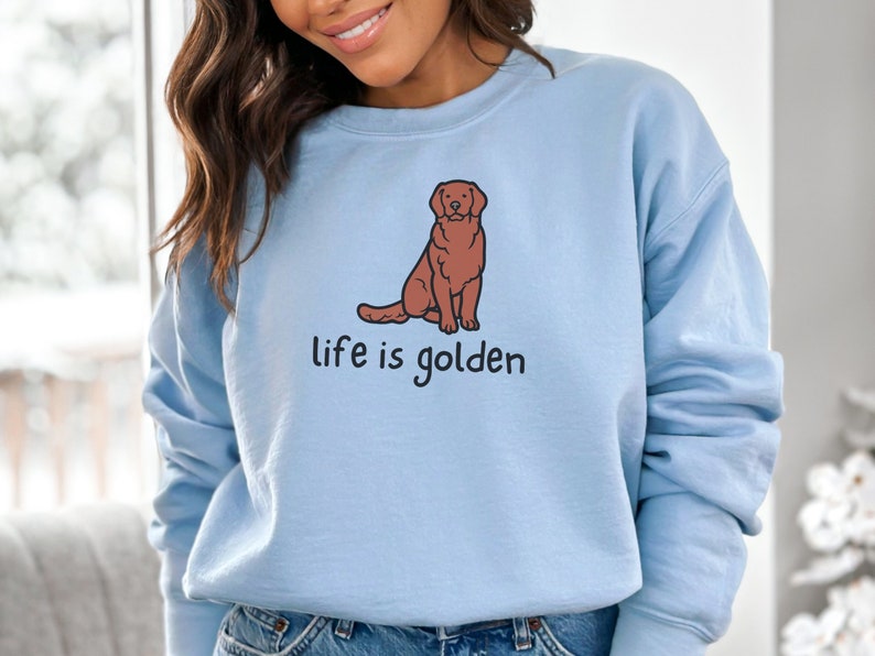 Op de afbeelding: Een lichtblauw sweatshirt met een afbeelding van een zittende golden retriever. De tekst "life is golden" staat onder de hond.