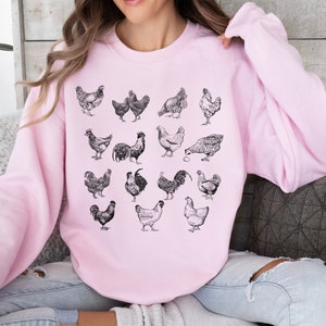 May include: A pink sweatshirt with a black and white illustration of various chickens and roosters. The illustration is centered on the sweatshirt.