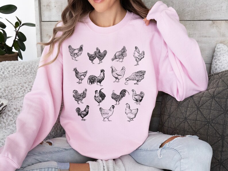 May include: A pink sweatshirt with a black and white illustration of various chickens and roosters. The illustration is centered on the sweatshirt.