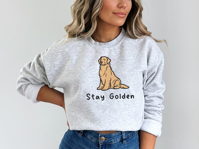 以下が含まれることがあります： 前面に卡通ゴールデンレトリバーが座っているイラストと「Stay Golden」という文字がプリントされたグレーのトレーナーです。