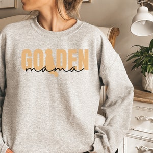 May include: A gray sweatshirt with the text "GOLDEN mama" in black and tan lettering.