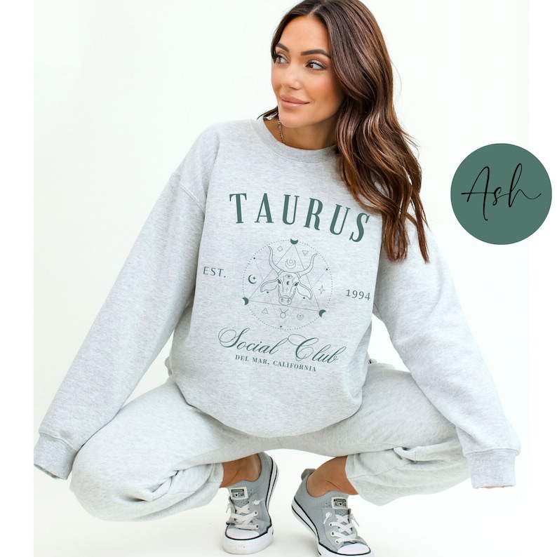 Puede incluir: Una sudadera gris con un dise&ntilde;o gr&aacute;fico verde que dice "Taurus Social Club Est. 1994 Del Mar, California".
