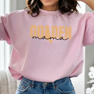 May include: A pink sweatshirt with the text "Golden mama" in a yellow-orange color.