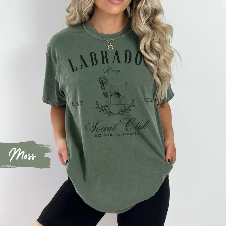 May include: A green t-shirt with a black graphic of a Labrador Retriever, the text "Labrador Social Club", and the words "Roxy Est. 2020 Del Mar, California".