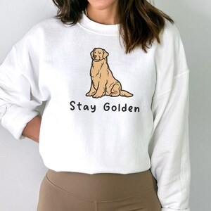 以下が含まれることがあります： 前面に卡通のゴールデンレトリバーが座っているイラストと「Stay Golden」という文字がプリントされた白いスウェットシャツです。