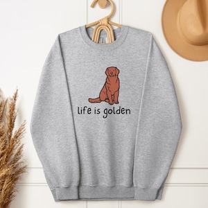 Op de afbeelding: Een grijs sweatshirt met een illustratie van een bruine golden retriever en de tekst "life is golden".