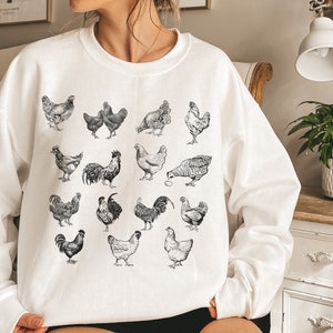 May include: White sweatshirt with a black and white illustration of various chickens and roosters.