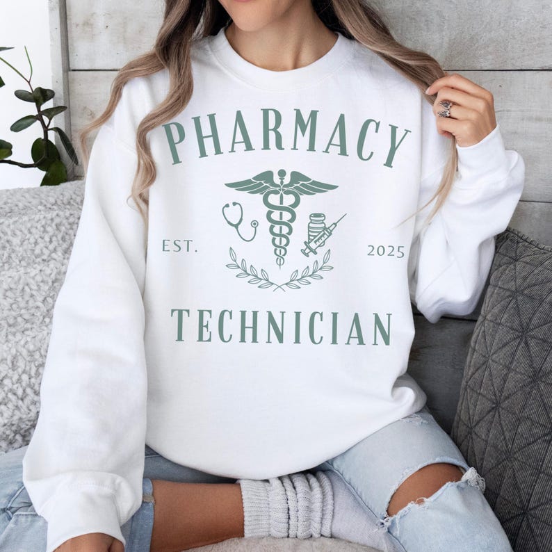 May include: White sweatshirt with the text "Pharmacy Technician" and a green medical symbol with a stethoscope, a bottle of pills, and a syringe. The text "Est. 2025" is below the symbol.