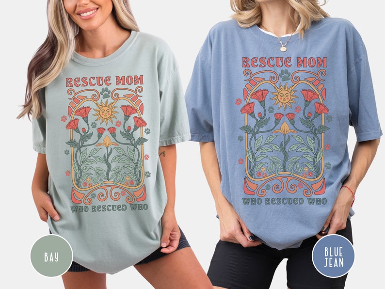 May include: Two women wearing oversized t-shirts with a vintage-style graphic design. The text on the shirts reads "Rescue Mom Who Rescued Who". The shirts are available in two colors: bay and blue jean.