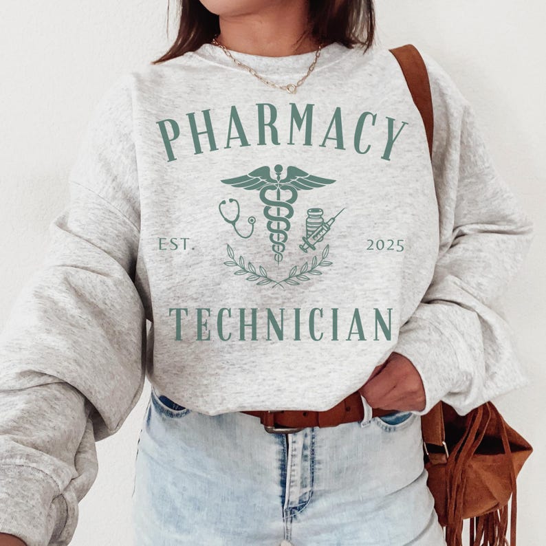 May include: A gray sweatshirt with the text "Pharmacy Technician" and a green caduceus symbol. The text "Est. 2025" is below the symbol.