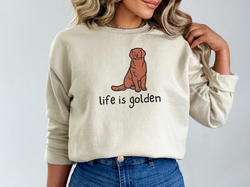 Op de afbeelding: Een beige sweatshirt met een cartoon golden retriever en de tekst "life is golden".