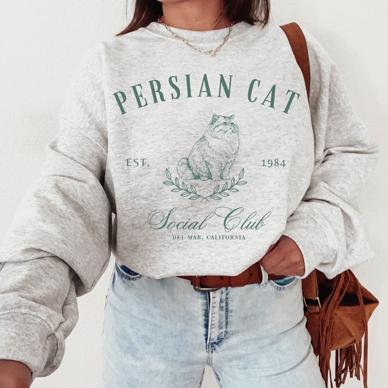 May include: A grey sweatshirt with a graphic of a Persian cat and the text "Persian Cat Social Club Est. 1984 Del Mar, California".
