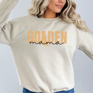 May include: A beige sweatshirt with the text "GOLDEN mama" in orange and black lettering.