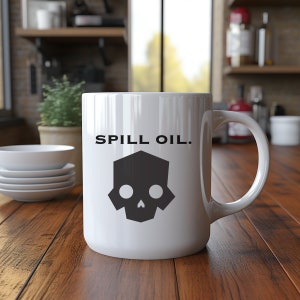 May include: White ceramic mug with a black geometric skull design and the text "SPILL OIL." The mug has a large handle and is sitting on a wooden surface. The background includes a kitchen setting.