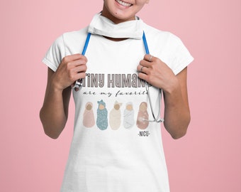 Può includere: Una maglietta bianca con il testo "Tiny Humans are my favorite -NICU-" e una grafica di cinque neonati avvolti in diversi colori.