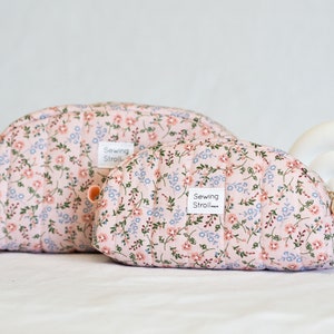 Könnte beinhalten: Zwei rosa gesteppte Kosmetiktaschen mit Blumenmuster und dem Text "Sewing Stroll" auf einem weißen Etikett.