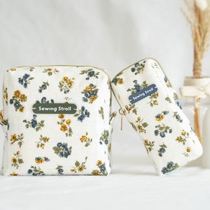 May include: Two white fabric zippered pouches with a floral pattern in blue and yellow. Both pouches have a green label with the text "Sewing Stroll" on them.