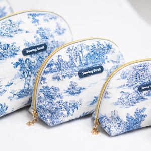 May include: A set of white and blue toiletry bags with a landscape design. The bags have gold zippers and a small blue tag that reads "Sewing Stroll". The bags are in various sizes.