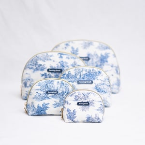 May include: A set of five cosmetic bags in varying sizes, featuring a blue and white toile pattern. Each bag has a gold zipper and a small rectangular label that reads "Sewing Street". The bags are arranged on a white background.