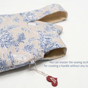 May include: A beige fabric tote bag with a blue and white floral pattern. The bag has a handle that is sewn into the fabric without any topstitching. A small red heart-shaped tag with the text "Just Sew" is attached to the bag.