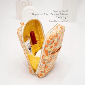 Puede incluir: Neceser abierto con estampado floral y cremallera, que contiene cosméticos. La bolsa es amarilla con flores naranjas y blancas. El interior es amarillo con bolsillos. El texto de la imagen dice "Sewing Stroll Organizer Pouch Sewing Pattern 'Molly' Original by Sewing Stroll."