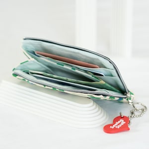 May include: A green and white patterned zippered pouch with a red heart keychain that says "Sewing Stuff". The pouch is open and has several cards and bills inside.