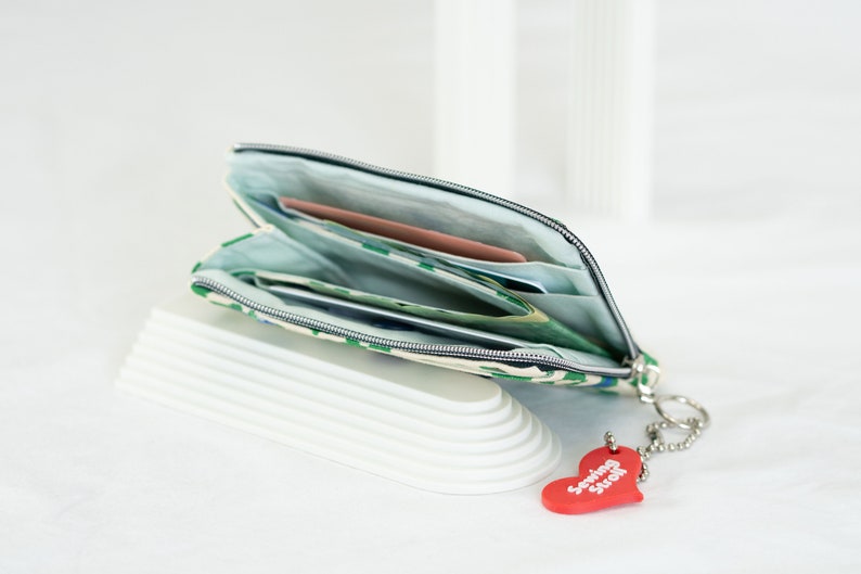 May include: A green and white patterned zippered pouch with a red heart keychain that says "Sewing Stuff". The pouch is open and has several cards and bills inside.