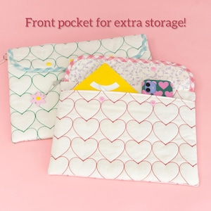 Puede incluir: Dos bolsas de tela blanca con patrones de corazones. Una tiene corazones rojos, la otra verdes. Las bolsas tienen un bolsillo frontal y est&aacute;n decoradas con detalles florales. Una bolsa contiene un objeto amarillo y un tel&eacute;fono.