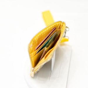 Puede incluir: Una cartera de tela amarilla con cierre de cremallera y un patr&oacute;n de lunares. La cartera est&aacute; abierta y tiene varias tarjetas dentro.