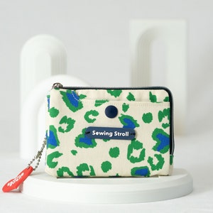 May include: A small, white canvas zippered pouch with a green and blue leopard print design. The pouch has a blue button and a blue label that reads "Sewing Stroll".