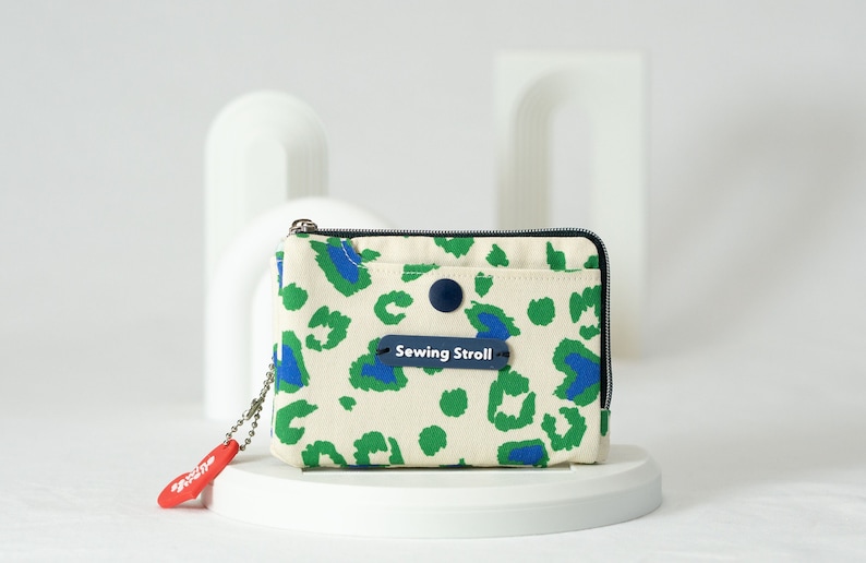 May include: A small, white canvas zippered pouch with a green and blue leopard print design. The pouch has a blue button and a blue label that reads "Sewing Stroll".