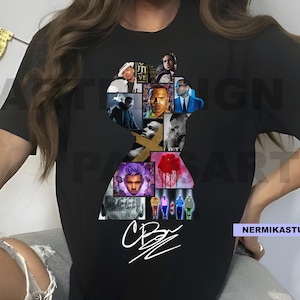 Op de afbeelding: Zwart t-shirt met een silhouetvormige collage van afbeeldingen. De collage bevat portretten en een witte handtekening. Het t-shirt heeft een ronde hals.