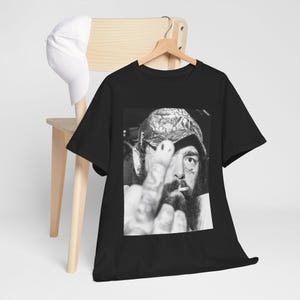 May include: Black t-shirt with a black and white photo of a man wearing a camouflage hat and giving the middle finger.
