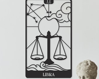 May include: Black metal Libra zodiac sign wall art. The design features scales, constellations, and the word "LIBRA". The artwork is displayed on a white wall, alongside decorative items like a bust, vases, and woven wall decor.