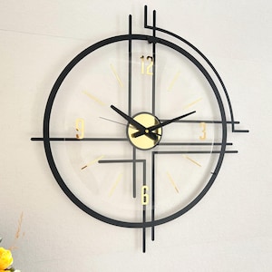 May include: A modern wall clock with a black frame and gold accents. The clock face is clear, with gold numerals and hands. The clock's design incorporates geometric shapes and lines, creating a contemporary aesthetic. The clock measures approximately 12 inches in diameter.