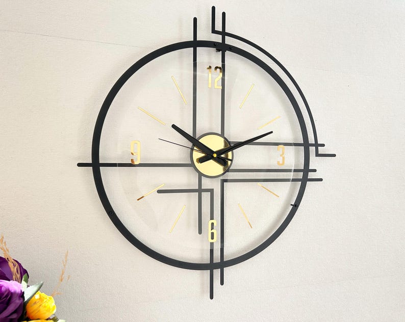 May include: A modern wall clock with a black frame and gold accents. The clock face is clear, with gold numerals and hands. The clock's design incorporates geometric shapes and lines, creating a contemporary aesthetic. The clock measures approximately 12 inches in diameter.