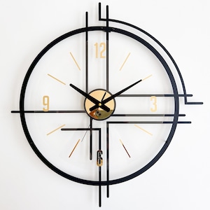 Puede incluir: Un reloj de pared moderno con esfera transparente, marco negro y detalles dorados. El reloj presenta números dorados en el 3, 6, 9 y 12, con manecillas negras. El diseño incorpora formas y líneas geométricas.