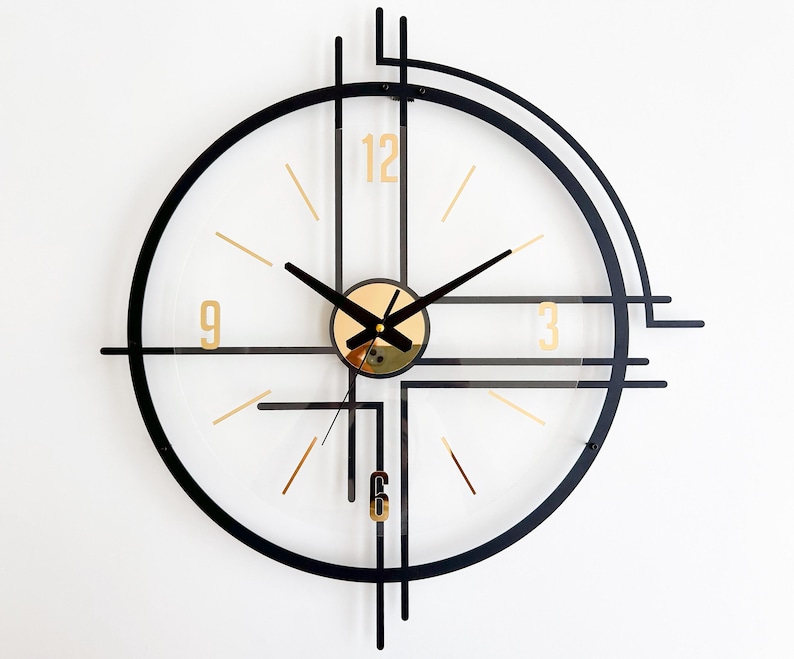 May include: A modern wall clock with a transparent face, black frame, and gold accents. The clock features gold numerals at 3, 6, 9, and 12, with black hands. The clock's design incorporates geometric shapes and lines.