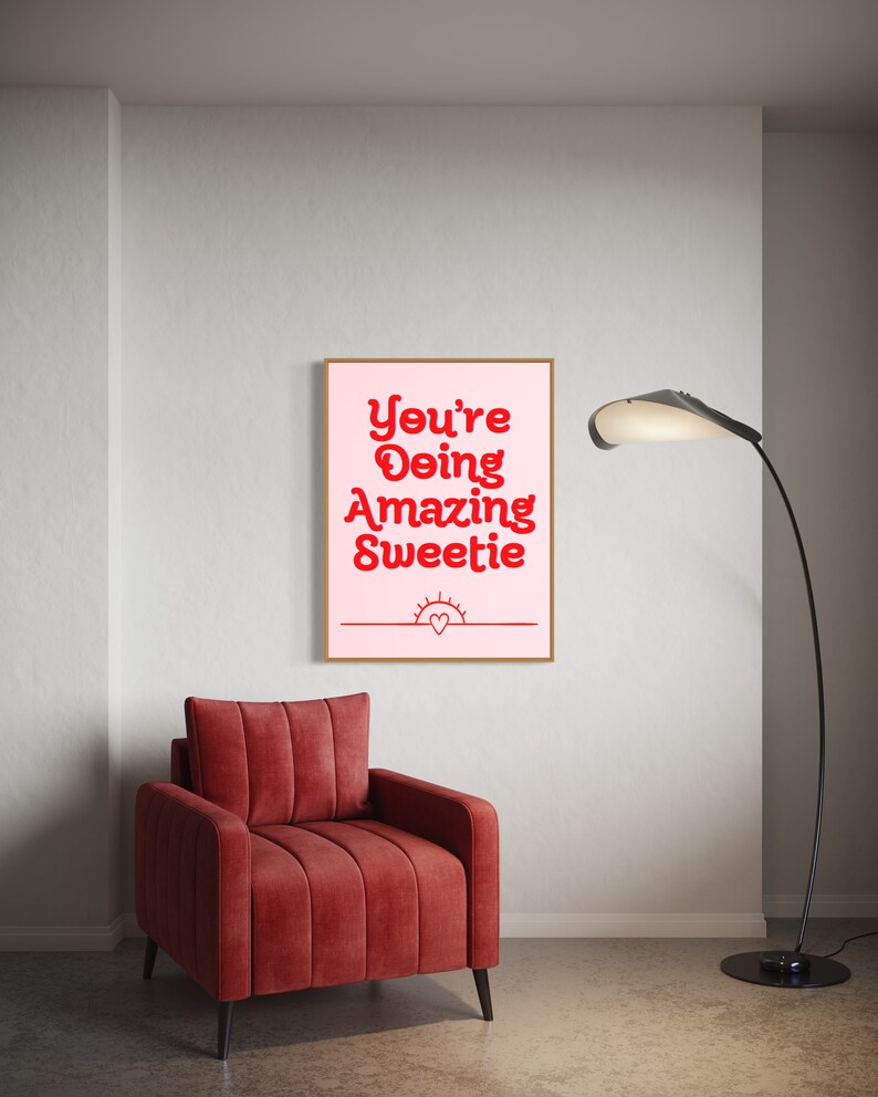 Puede incluir: Una impresi&oacute;n enmarcada rosa y blanca con el texto "You're Doing Amazing Sweetie" en rojo. La impresi&oacute;n est&aacute; colgada en una pared blanca sobre un sill&oacute;n rojo.