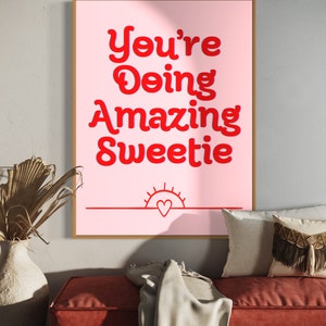 Puede incluir: Un p&oacute;ster motivacional rosa y rojo con el texto "You're Doing Amazing Sweetie" en una fuente retro. Un peque&ntilde;o coraz&oacute;n rojo est&aacute; dentro de un gr&aacute;fico de sol en la parte inferior del p&oacute;ster.