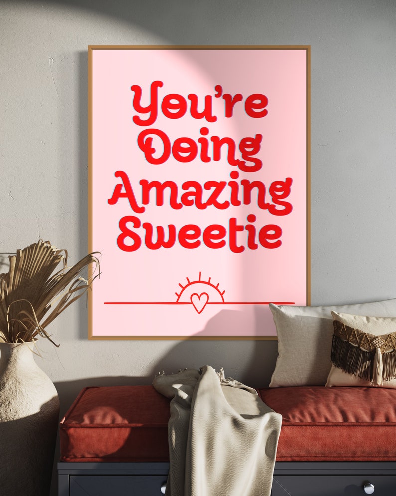 Puede incluir: Un p&oacute;ster motivacional rosa y rojo con el texto "You're Doing Amazing Sweetie" en una fuente retro. Un peque&ntilde;o coraz&oacute;n rojo est&aacute; dentro de un gr&aacute;fico de sol en la parte inferior del p&oacute;ster.