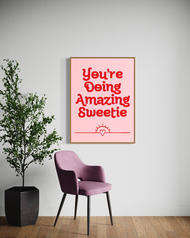 Puede incluir: Una impresi&oacute;n enmarcada rosa con el texto "You're Doing Amazing Sweetie" en letras rojas. Un peque&ntilde;o sol con un coraz&oacute;n dentro est&aacute; debajo del texto.